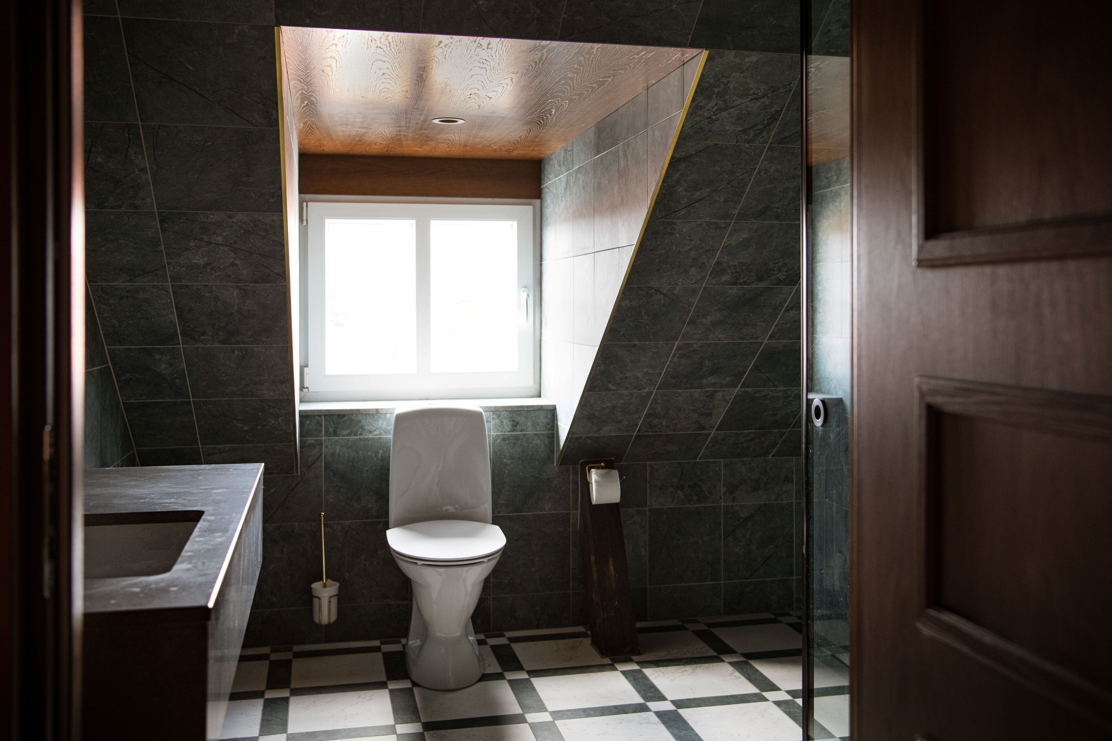 A bathroom with a checkered floor, a toilet, a window, and a wooden door.