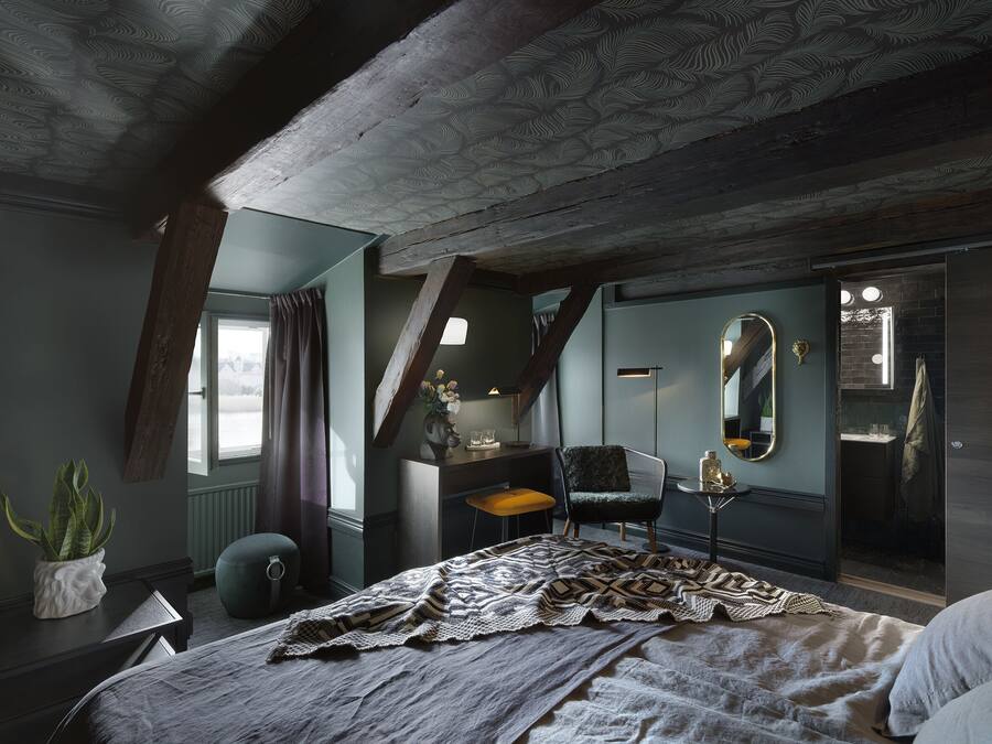 A bedroom with a large bed, a chair, a desk, a mirror, and a window with curtains.