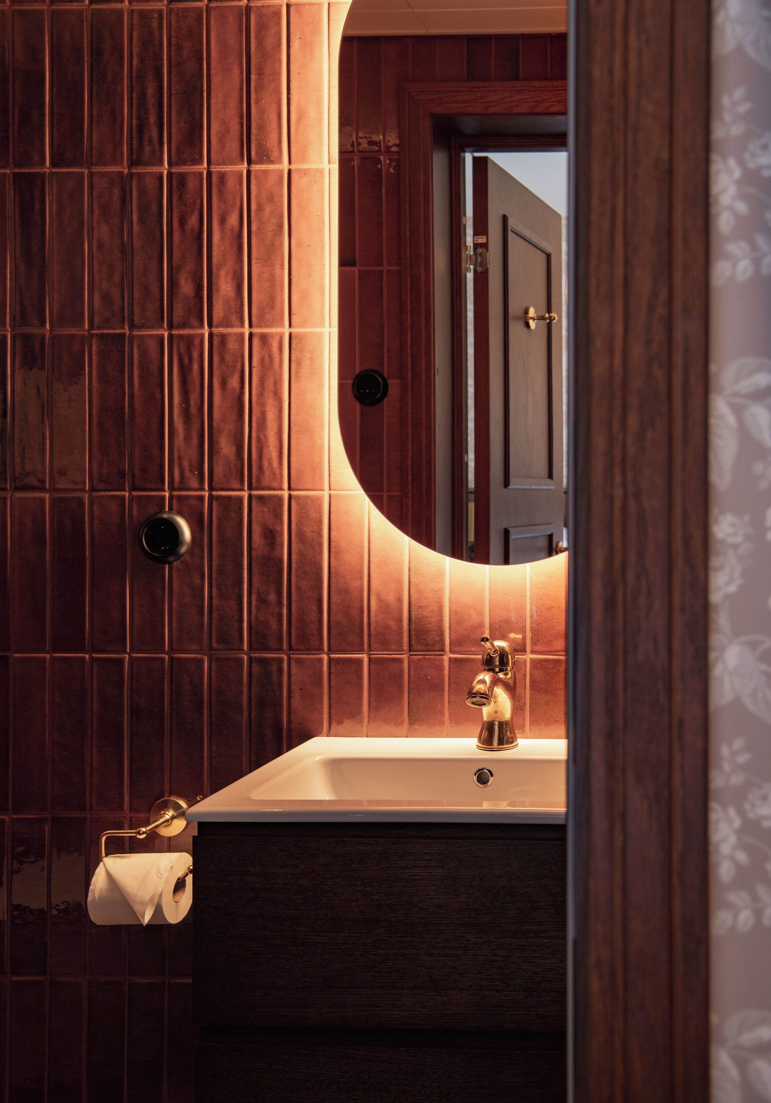 Un baño con pared de madera, un lavamanos con grifo dorado y un dispensador de papel higiénico.