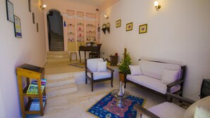 A living room with a sofa, chairs, a coffee table, and a bookshelf. There is a staircase leading to another room. - Kleo Pension (Kas)