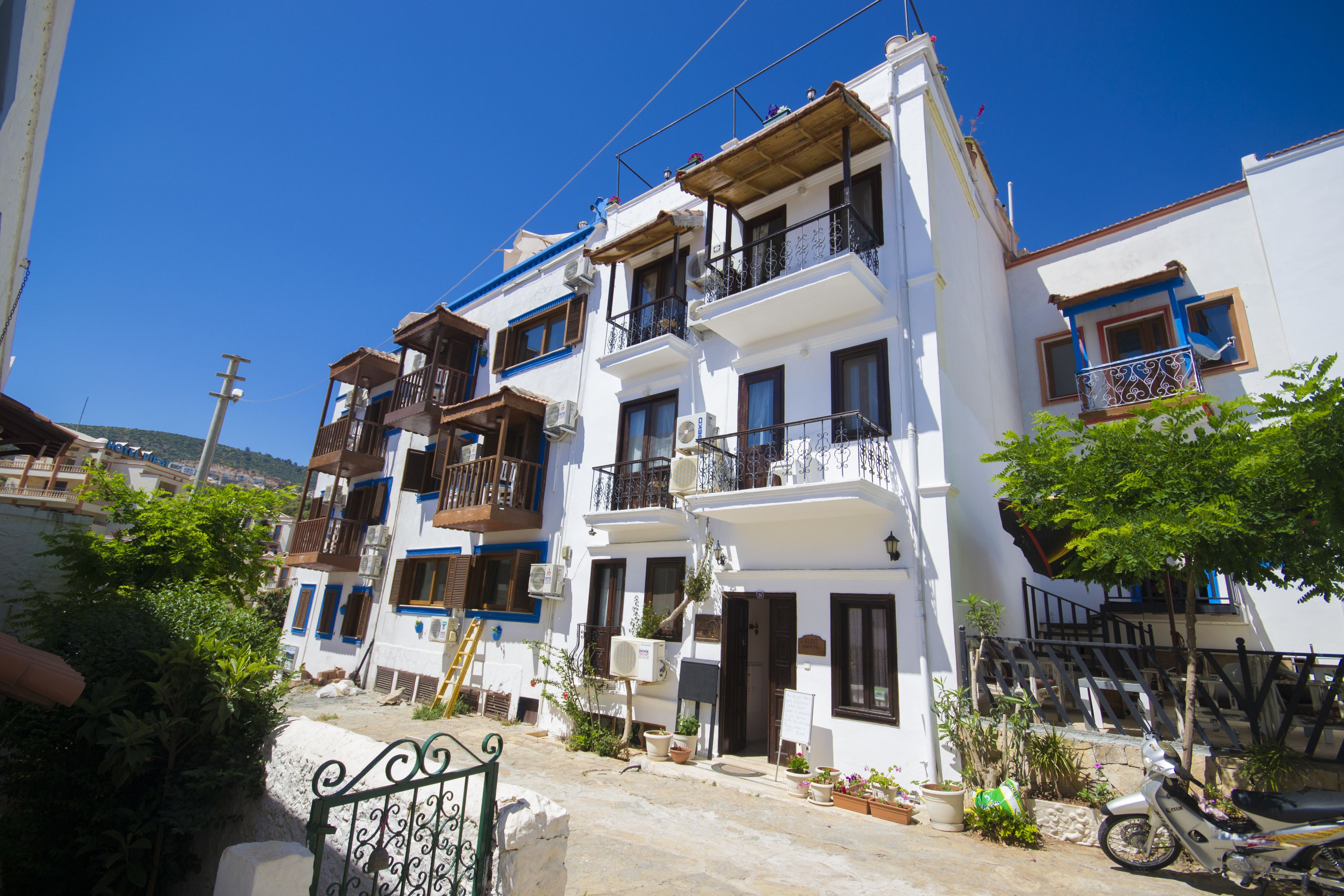 A row of white buildings with balconies, some with plants, and a motorcycle parked in front.