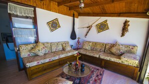 A cozy living room with a wooden ceiling, a floral sofa, a small round table with a hookah, and decorative wall hangings. - Kleo Pension (Kas)
