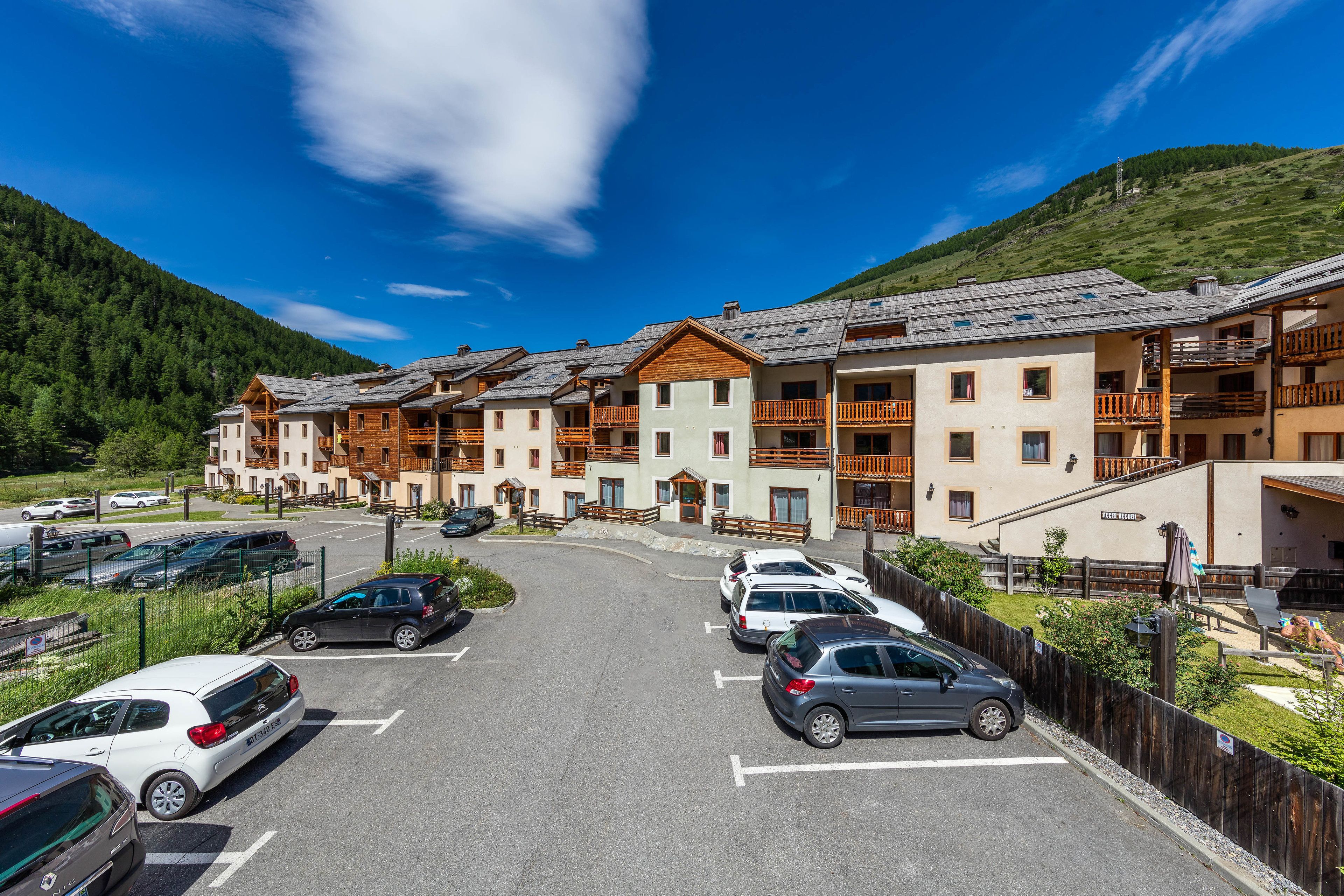 A multi-story hotel with a parking lot, surrounded by mountains and greenery.