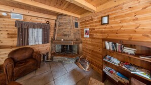 A cozy log cabin interior with a stone fireplace, a leather armchair, and a bookshelf filled with books. - Noemys Les Balcons du Viso  (Abriès-Ristolas)