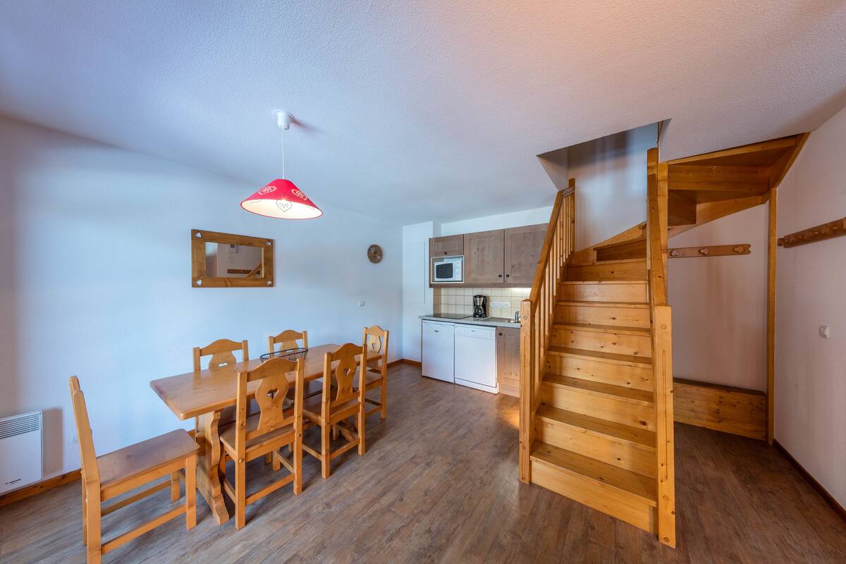 Una cocina compacta con armarios de madera, un comedor con mesa y sillas, y una escalera de madera.