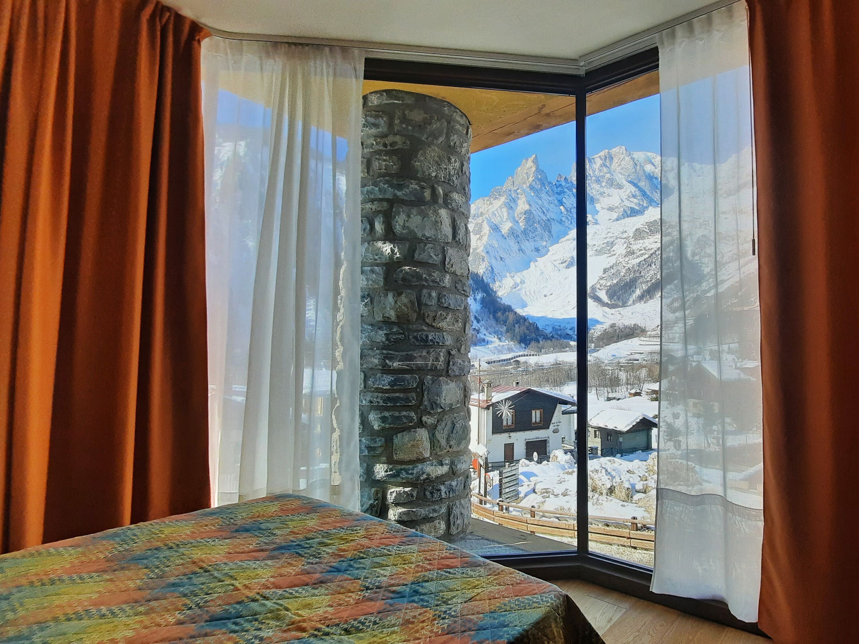 A room with a bed, a stone pillar, and a view of snow-covered mountains. - Hotel Aigle (Courmayeur)