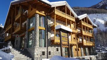 Ein Holzgebäude mit einer Steinaußenfassade, das als Hotel und Restaurant ausgeschildert ist. Es hat große Fenster und eine Treppe, die zum Eingang führt.