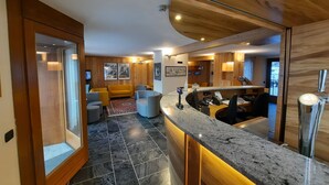 A modern interior with a wooden ceiling, a marble countertop, and a seating area with a yellow sofa and grey armchairs. - Hotel Aigle (Courmayeur)