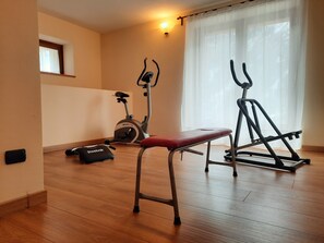 A room with wooden flooring, a standing bike, a stationary bike, and a bench. - Hotel Aigle (Courmayeur)
