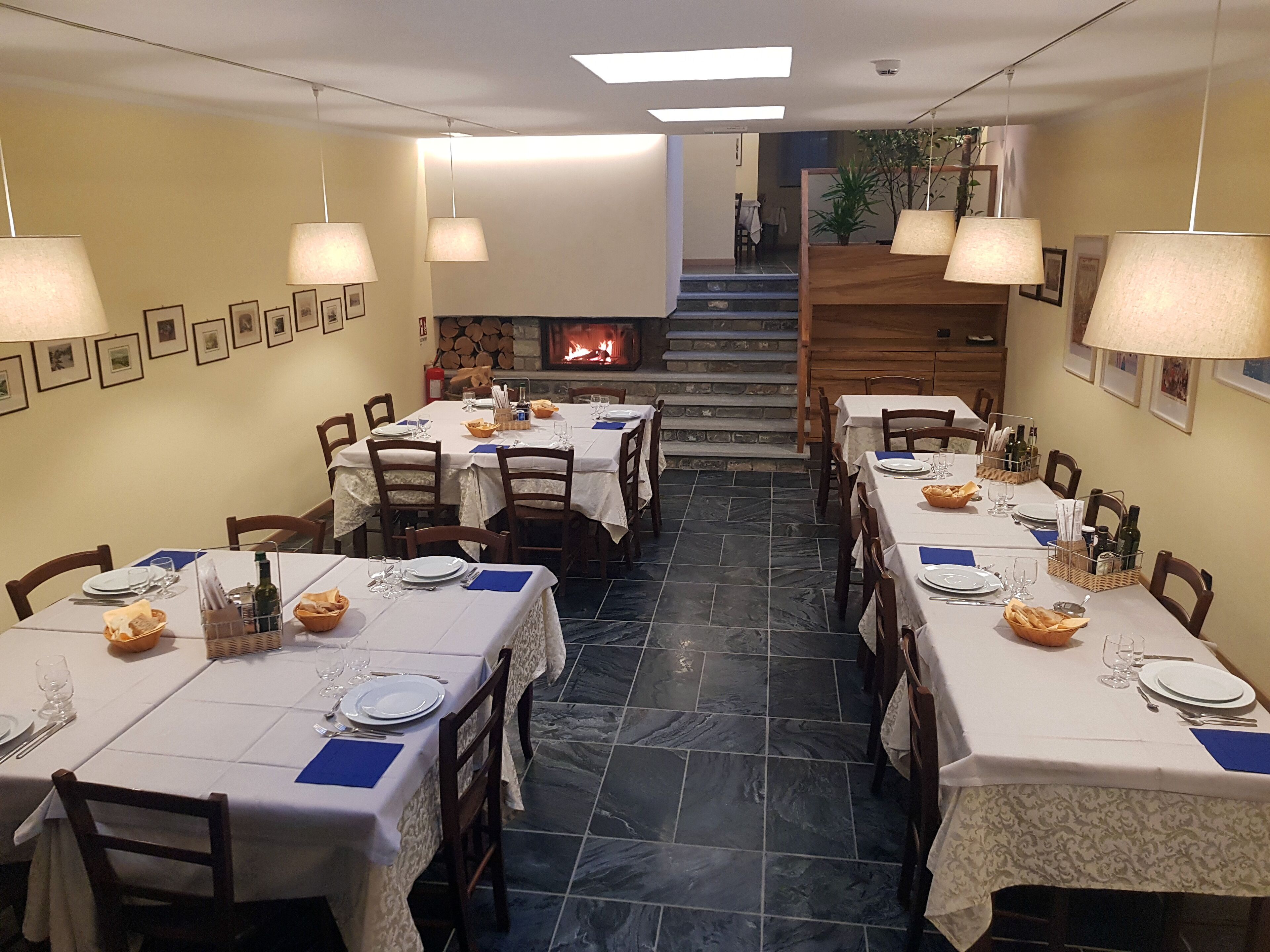 A dining area with tables set for meals, a fireplace, and a staircase leading to an upper level.