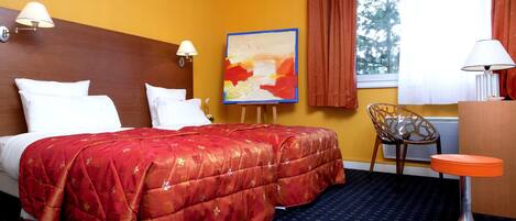 Una camera d'albergo con un letto, una sedia, un tavolino e un quadro appeso al muro.