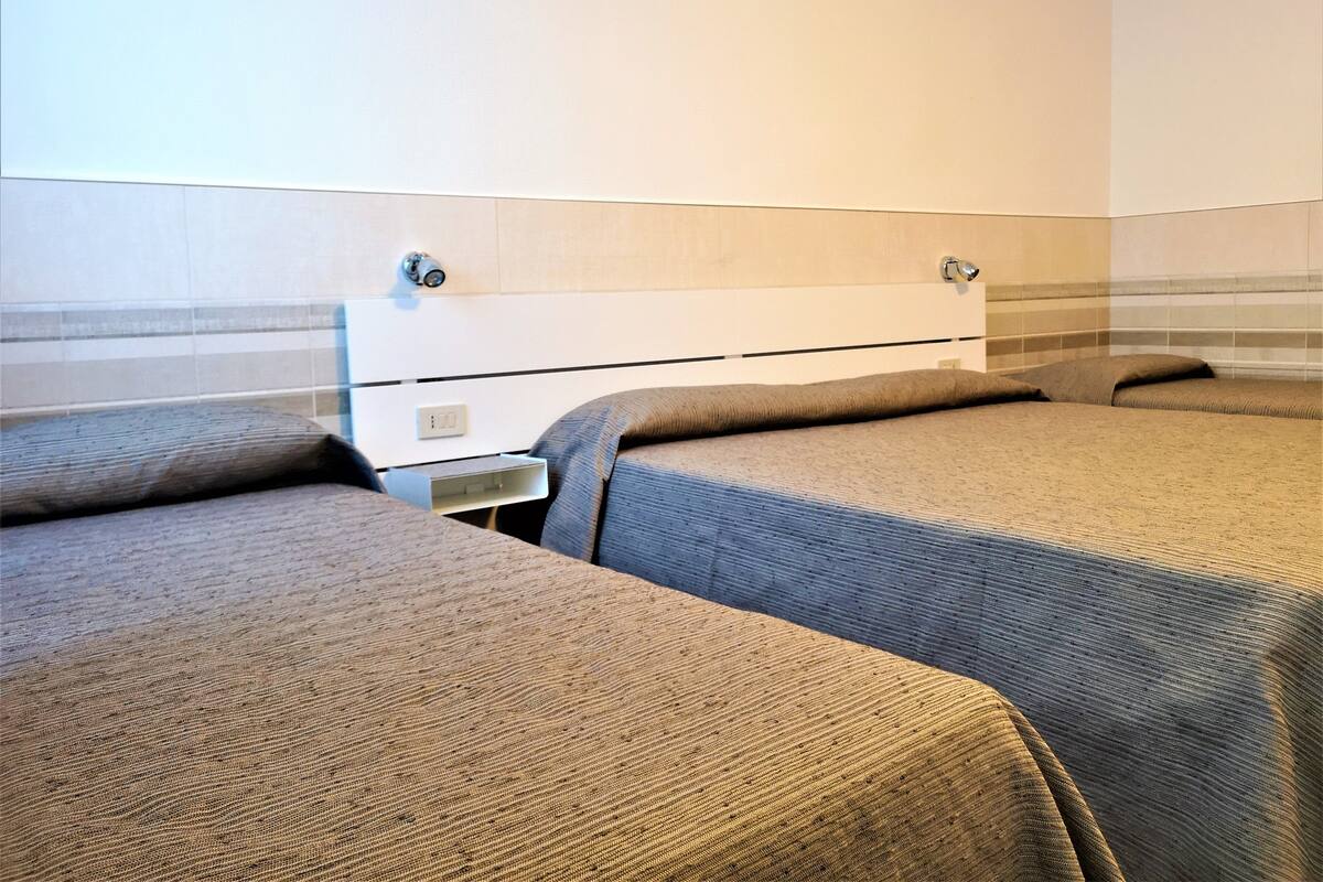 Habitación de hotel con dos camas individuales, una mesita de noche pequeña y un aire acondicionado instalado en la pared.