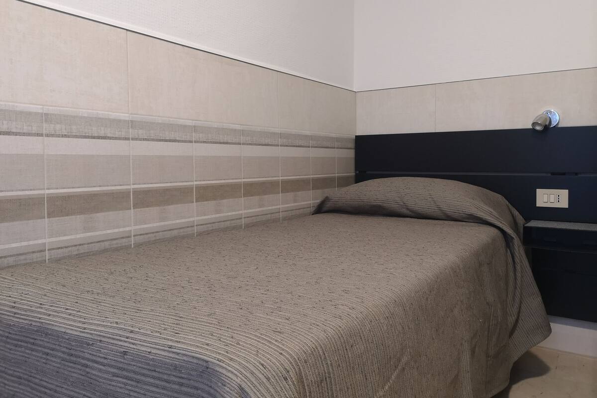 Un dormitorio pequeño y ordenado con una cama, una mesita de noche y una lámpara de pared.