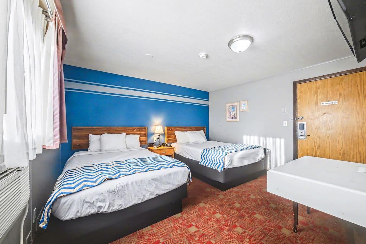 Hotellihuone, jossa on kaksi sänkyä, työpöytä, puuovi ja sininen seinä.