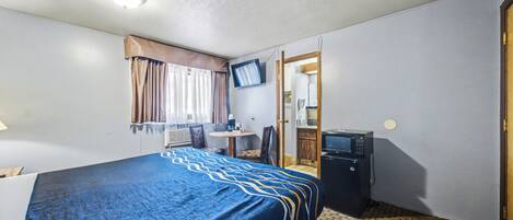Une chambre d’hôtel équipée d’un lit, d’un bureau, d’une télévision, d’un four à micro-ondes et d’une salle de bain visible à travers une porte ouverte.