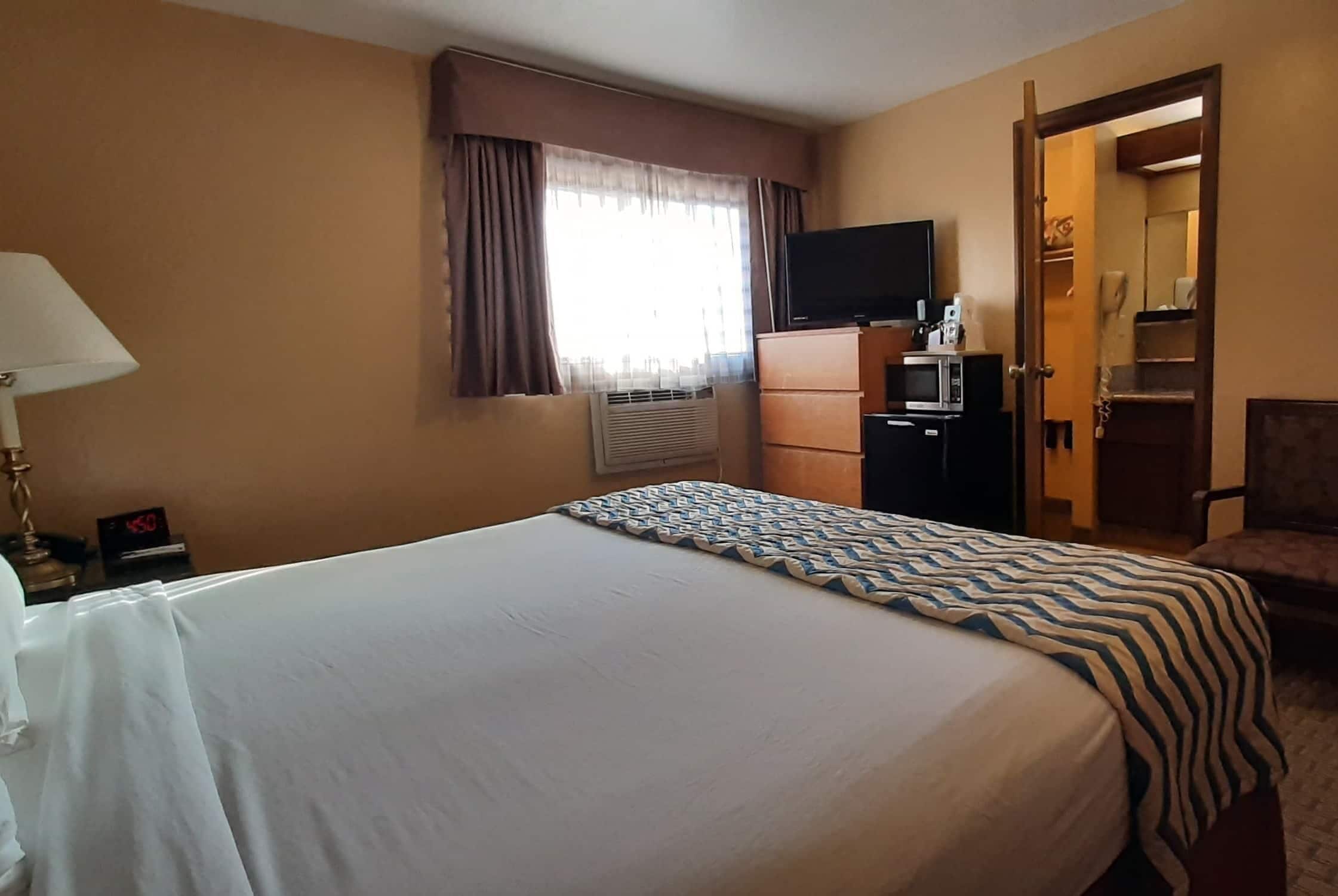 Habitación de hotel con cama, televisor sobre un mueble, escritorio con lámpara y armario.