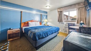Habitación de hotel con cama, mesita de noche, lámpara, ventana con cortinas y una pequeña mesa con sillas.