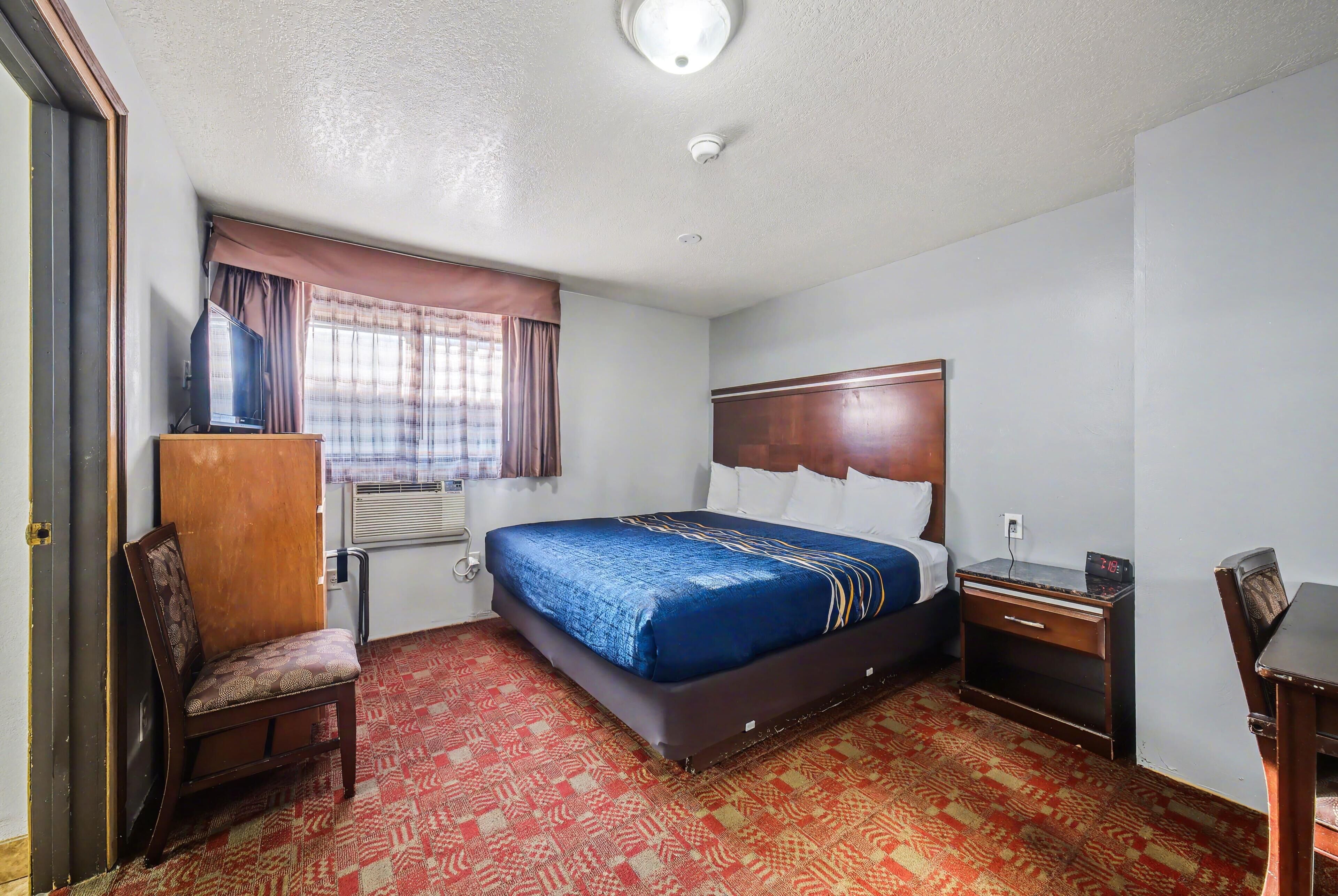 A hotel room with a bed, a chair, a desk, a wardrobe, and a window with curtains.