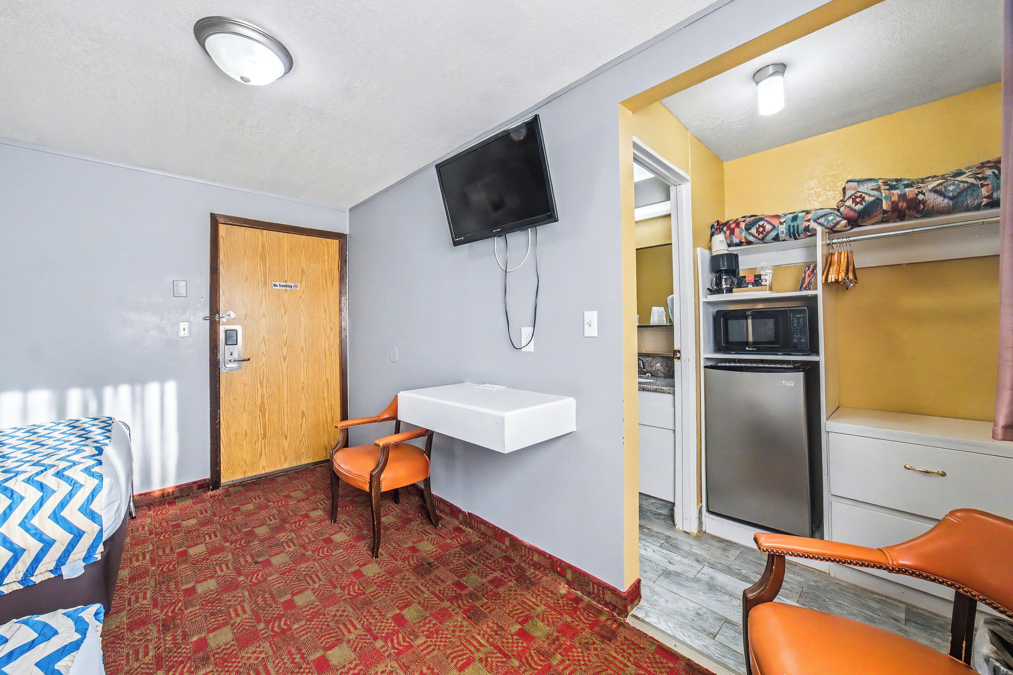 A room with a bed, a desk, a chair, a television, a microwave, and a kitchenette.