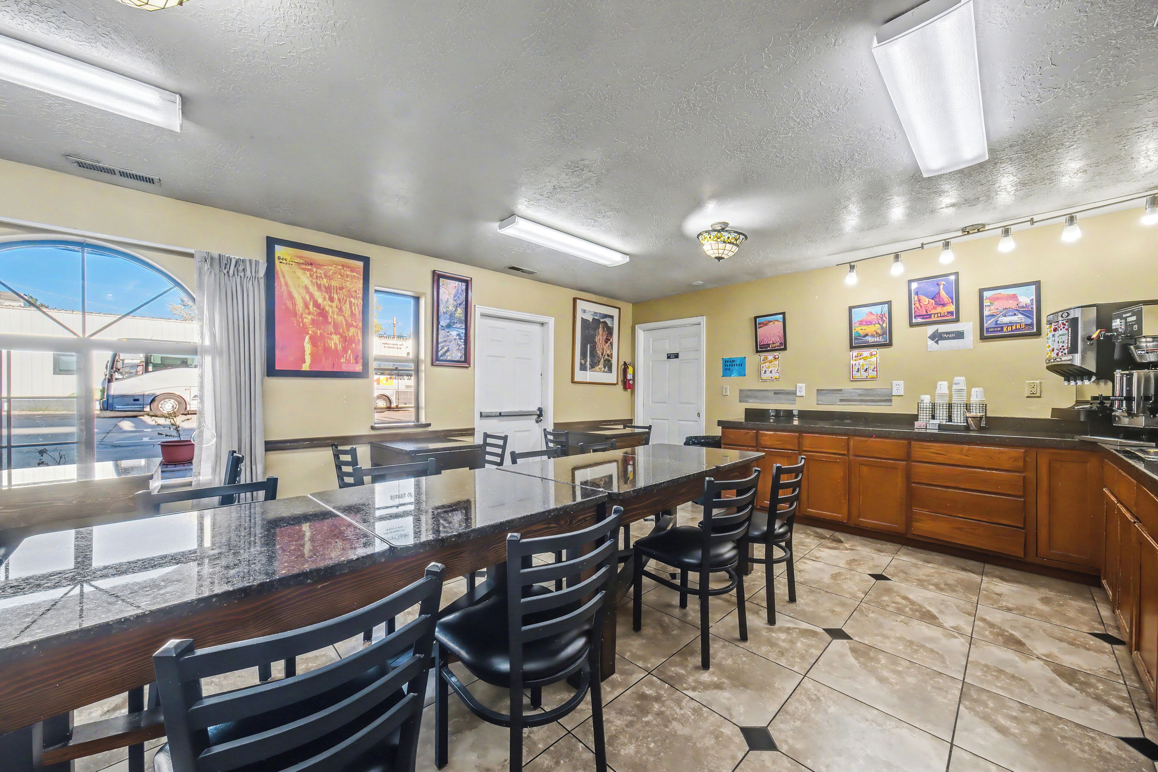 A kitchen with a large island, chairs, and a dining table. There are framed pictures on the wall and a view of the outside.