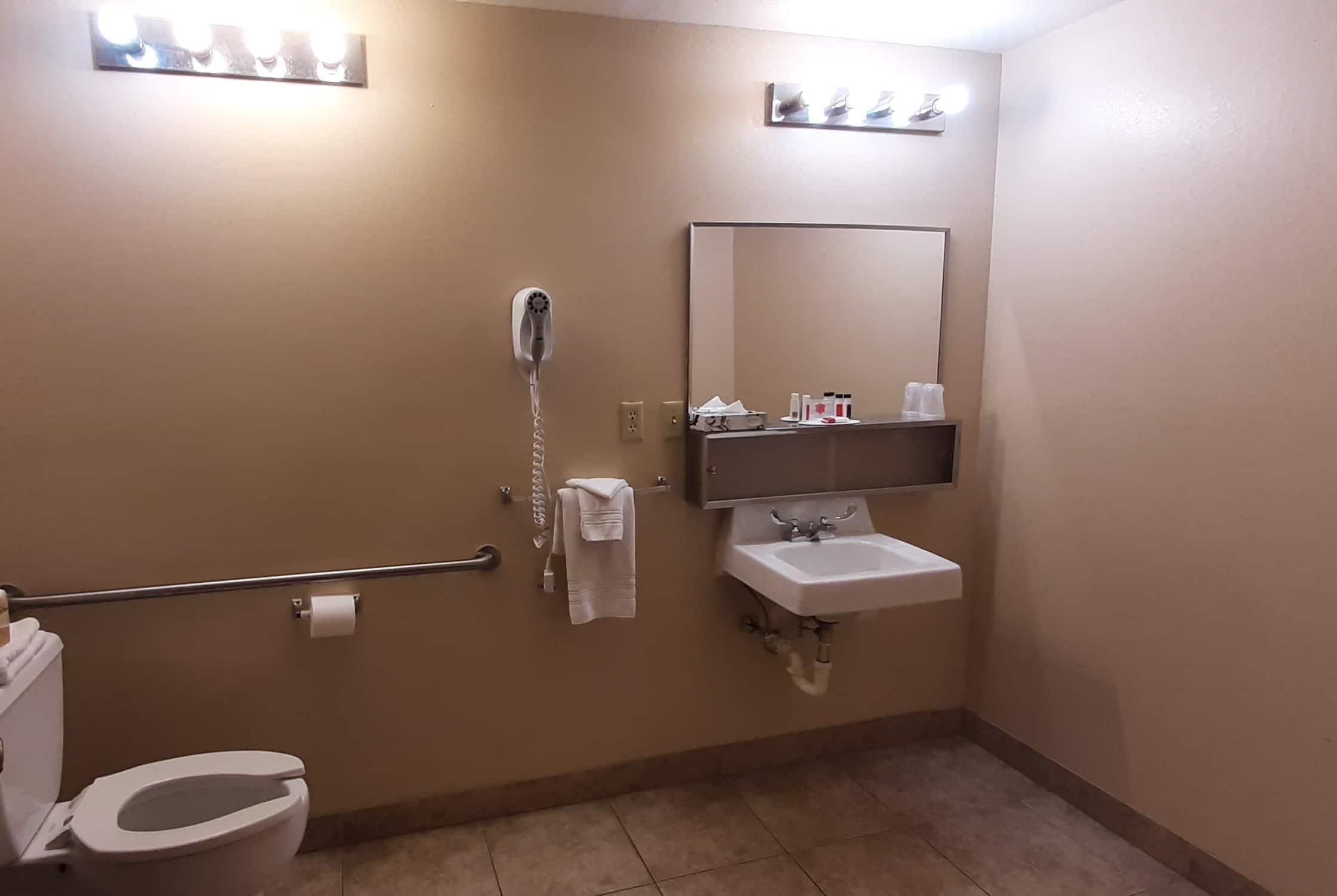 Une salle de bain équipée d’un WC, d’un sèche-mains, d’un porte-serviettes, d’un lavabo, d’un miroir et d’un distributeur de serviettes.
