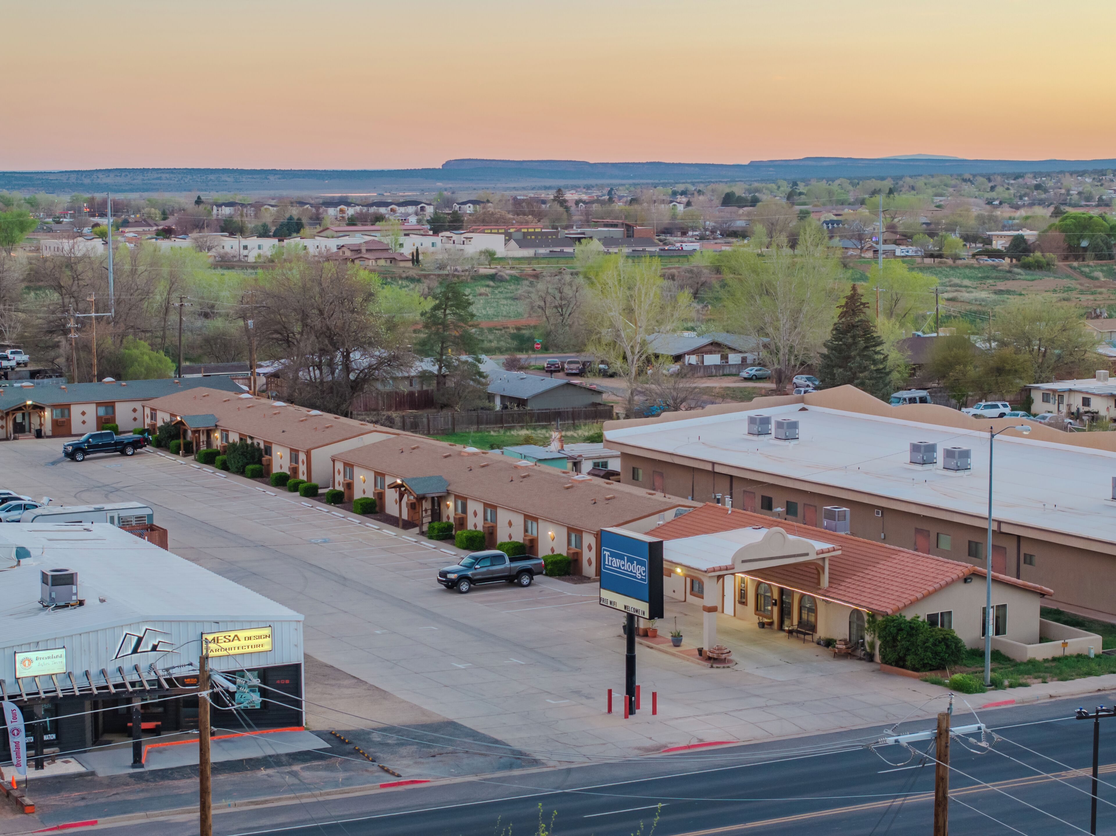 A travel lodge with a parking lot, a signboard, and a view of the surrounding area.