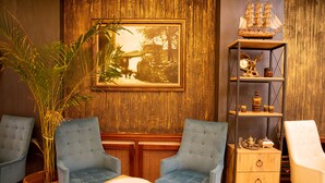 A room with two blue upholstered chairs, a wooden side table, a large potted plant, a wooden cabinet with drawers, and a framed picture on the wall. - Cumbali Luxury Boutique Hotel (Istanbul)