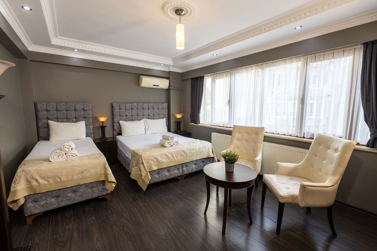 Een hotelkamer met twee bedden, een zithoek met een stoel, een tafeltje en een raam met gordijnen.