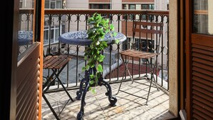 A balcony with a table and chairs, a potted plant, and a view of a multi-story building with air conditioning units. - Cumbali Luxury Boutique Hotel (Istanbul)