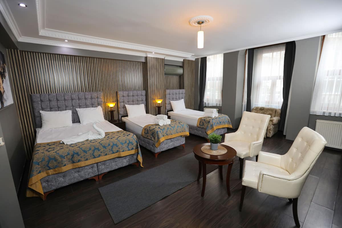 Een hotelkamer met twee bedden, een zithoek met een fauteuil en een tafeltje met een plant.
