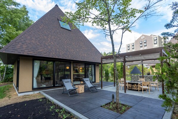 Una casa moderna con techo inclinado, grandes ventanales y un patio con mobiliario exterior.