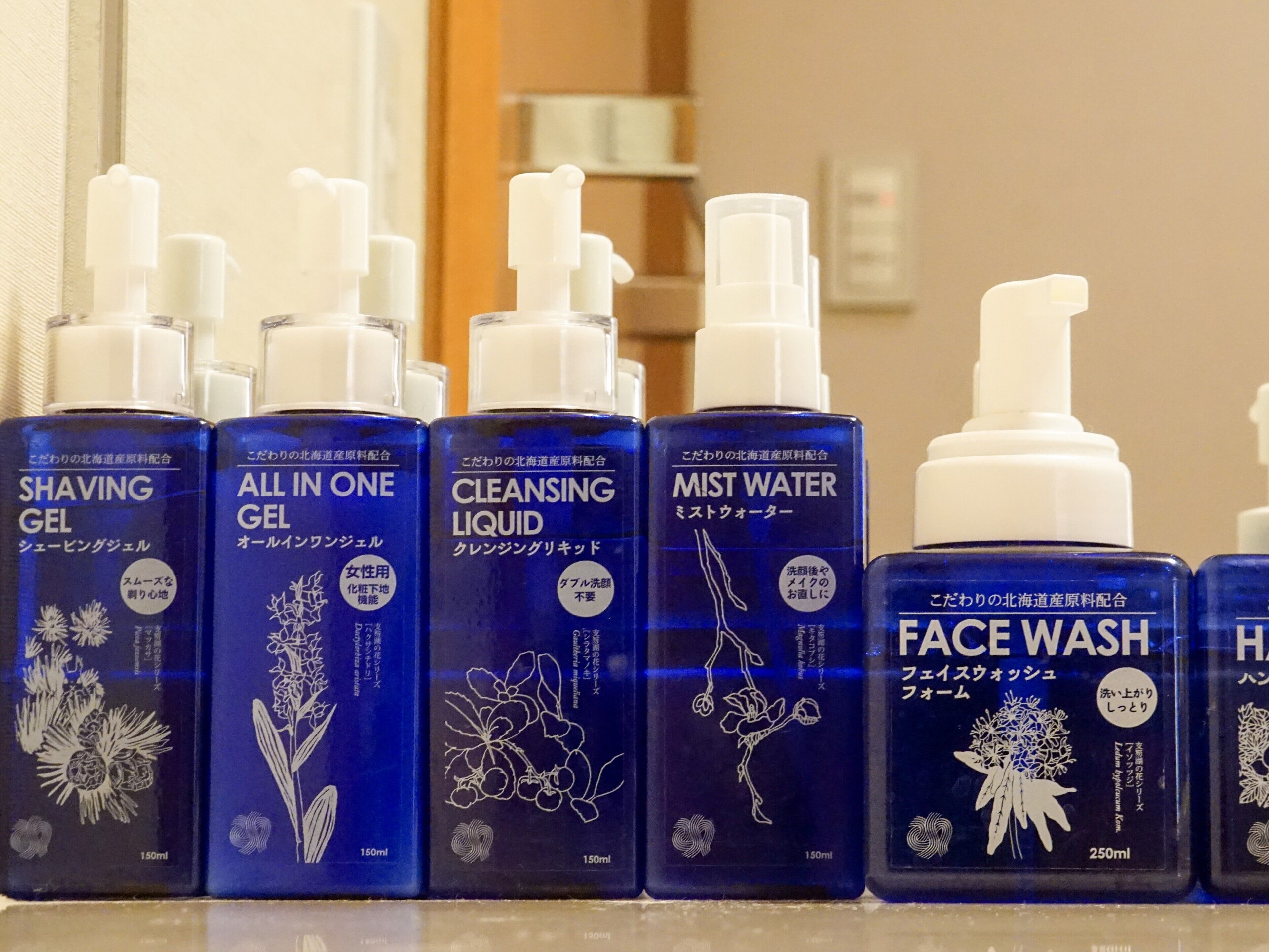 A row of personal care products including shaving gel, cleansing liquid, mist water, and face wash.