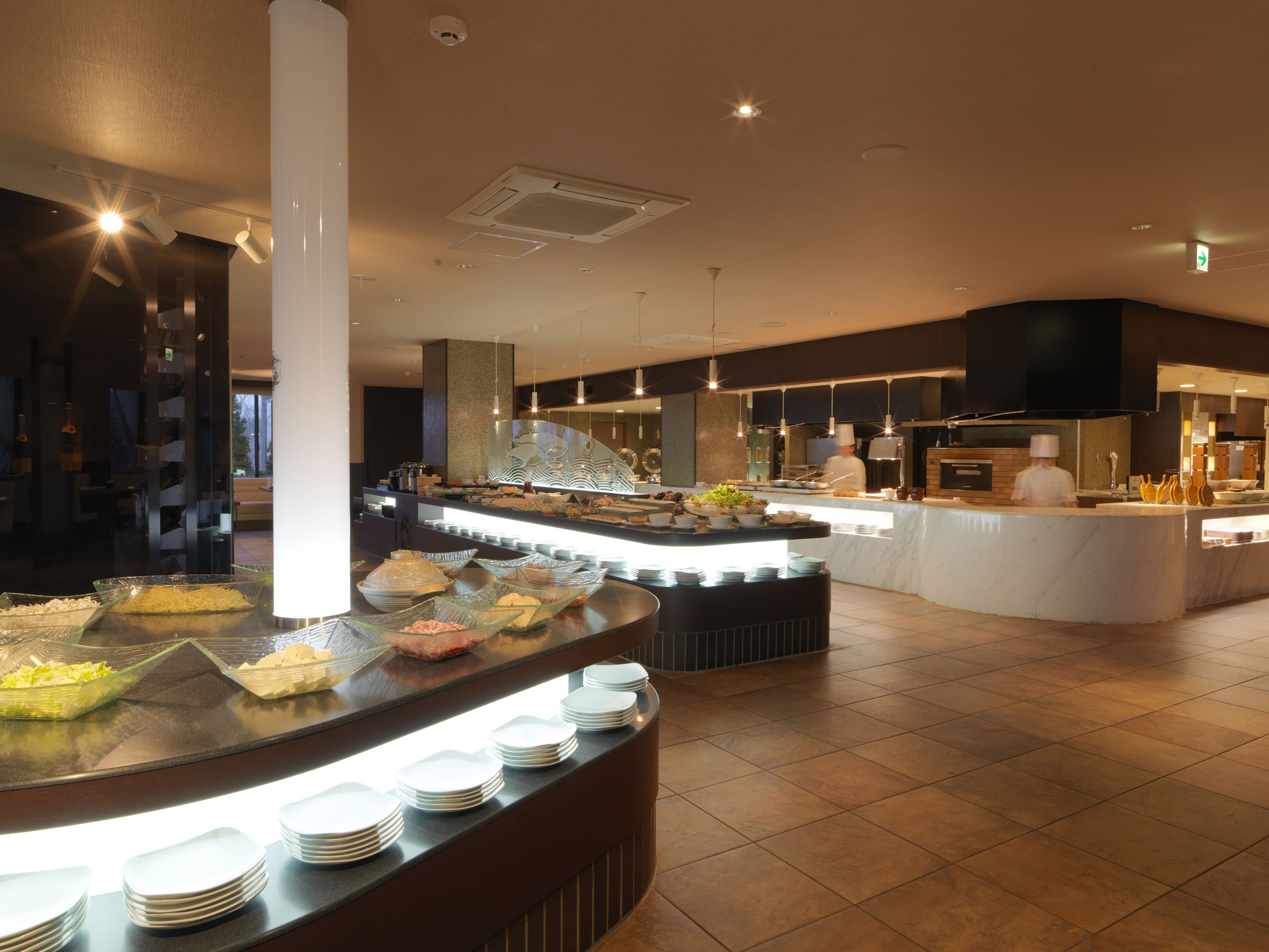 A buffet area with various food items and a chef preparing food in the background.