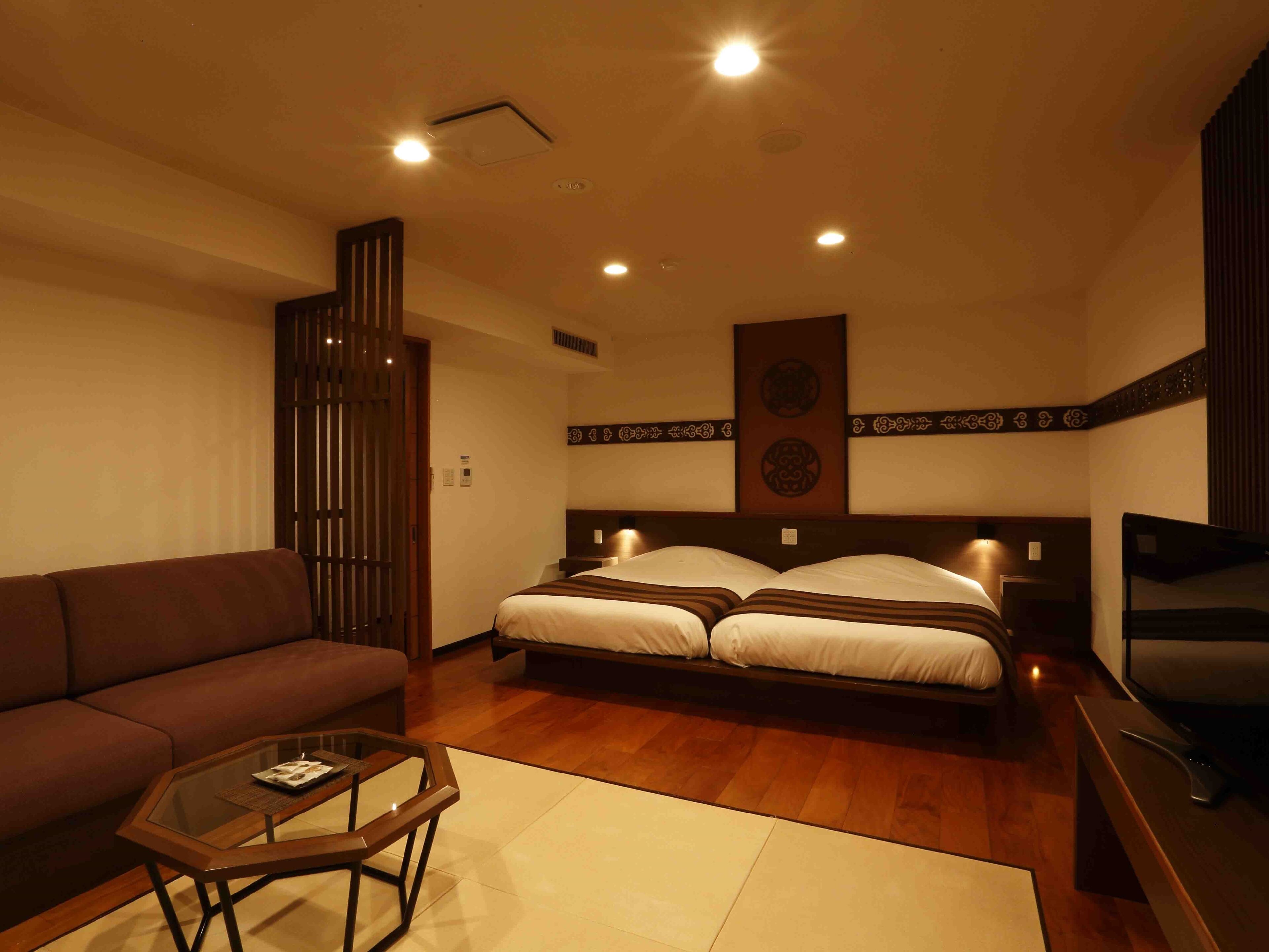 A hotel room with a bed, a sofa, a glass coffee table, and a TV.
