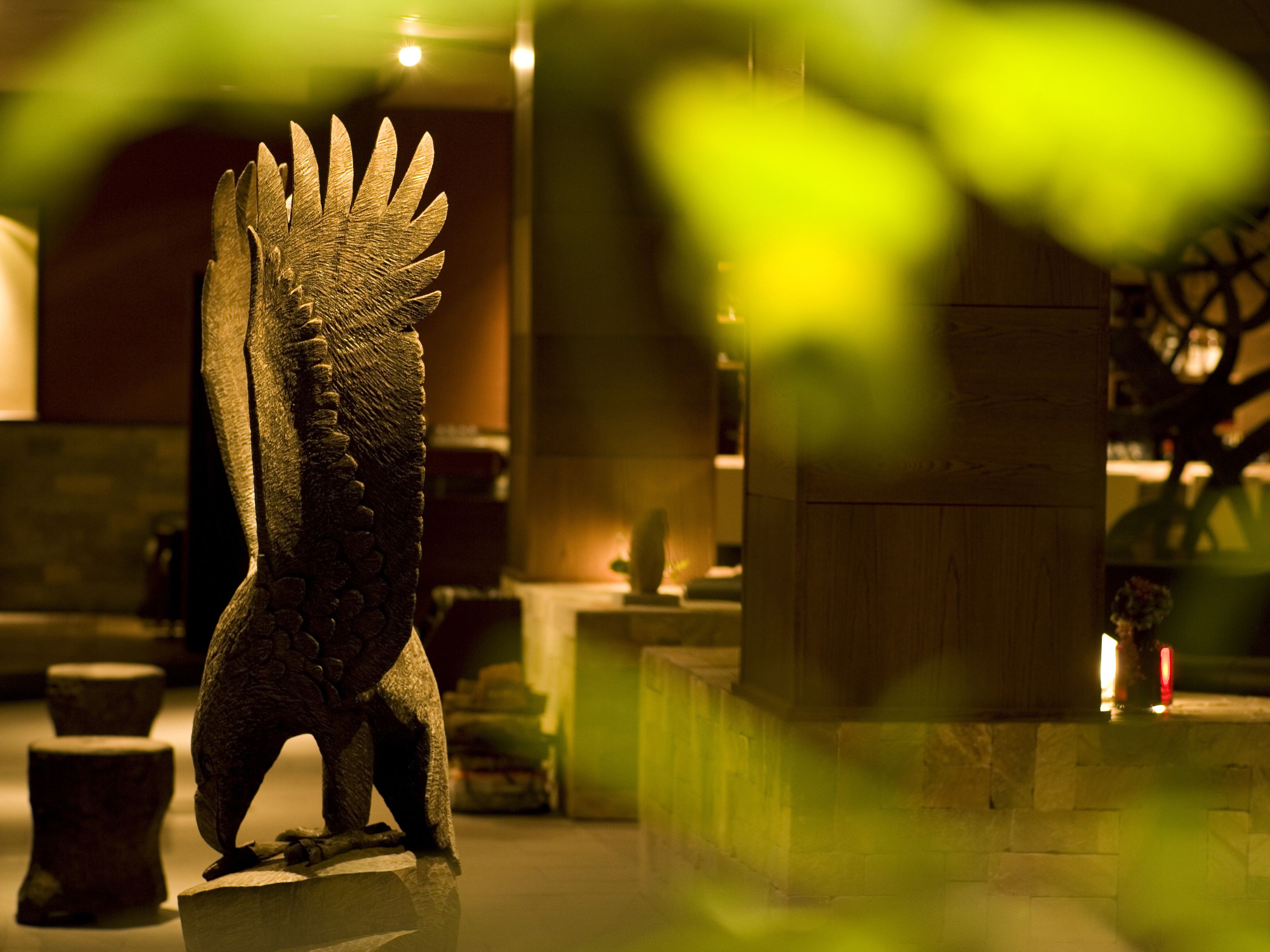 Una scultura in pietra raffigurante un uccello, in un ambiente interno ben illuminato con parete in pietra e pavimento in legno.