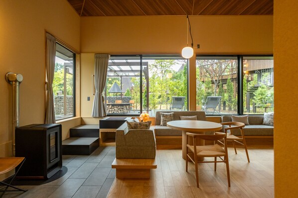 A modern living room with a fireplace, comfortable seating, and large windows offering a view of the outdoors.