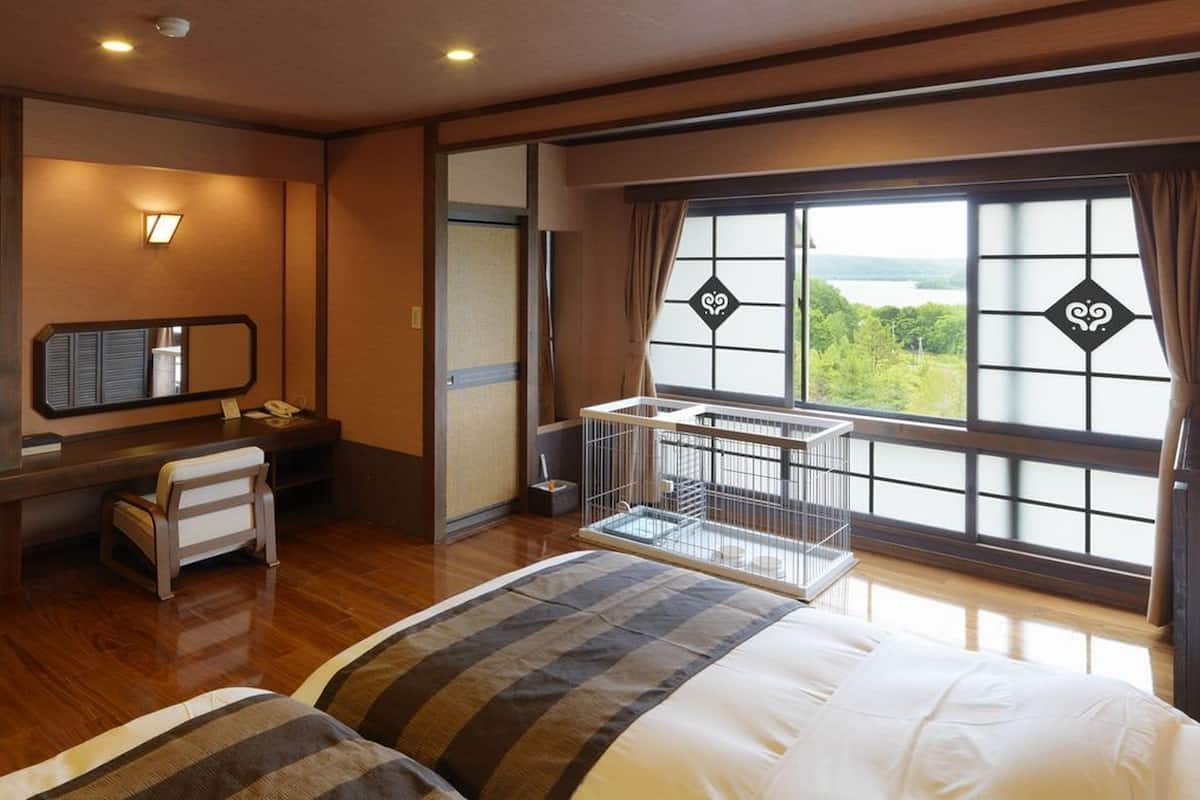 A hotel room with a bed, a desk with a chair, a TV, a safe, and a window with a view.
