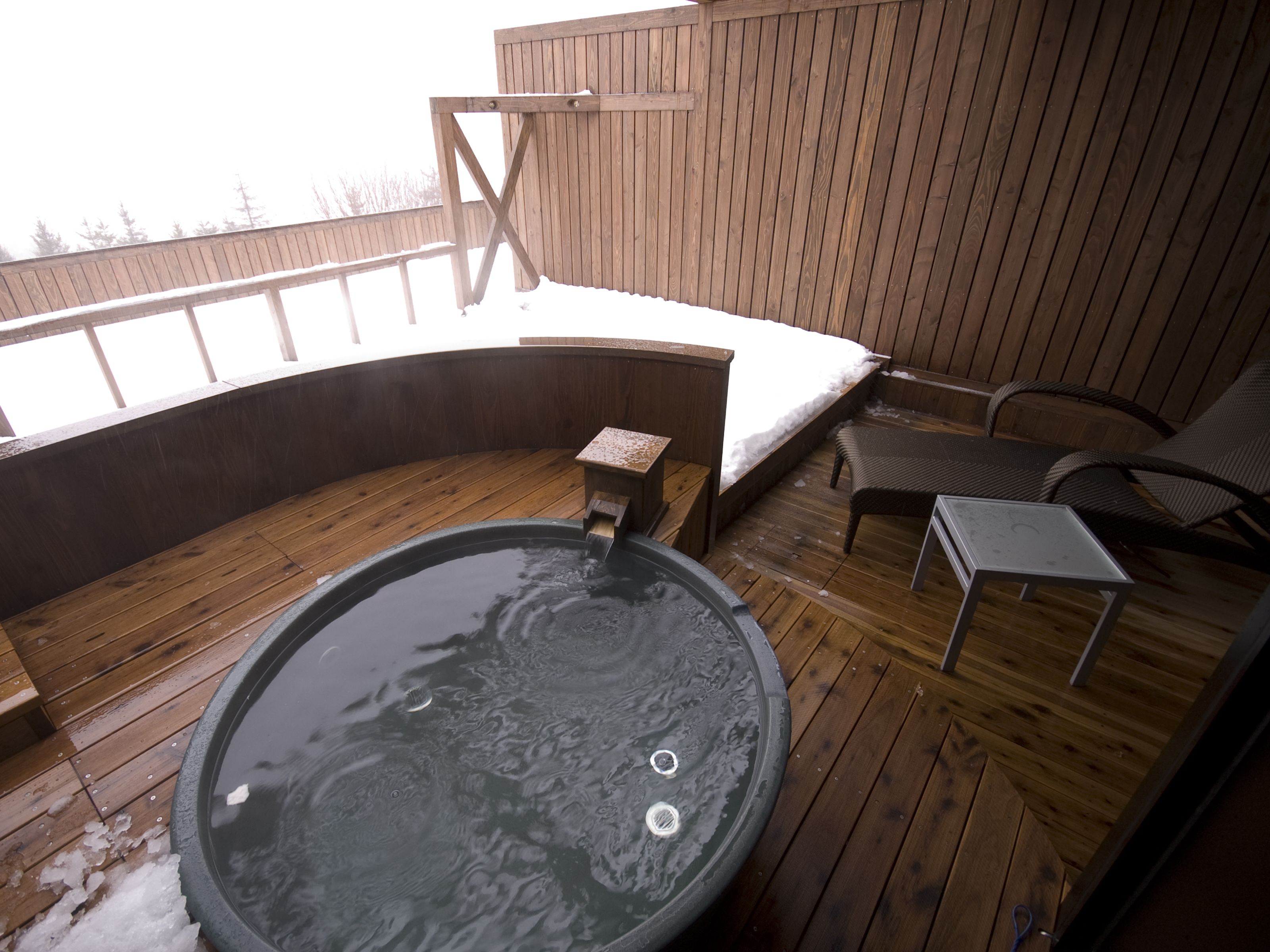 A wooden deck with a hot tub, a small table, and two chairs.