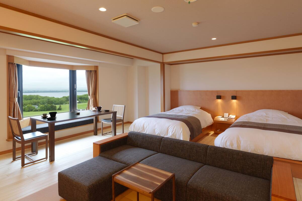 Habitación de hotel con un ventanal grande, un sofá, una mesita y dos camas.