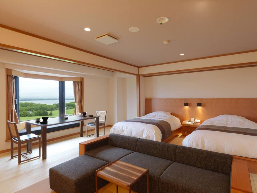 Habitación de hotel con un ventanal grande, un sofá, una mesita y dos camas.