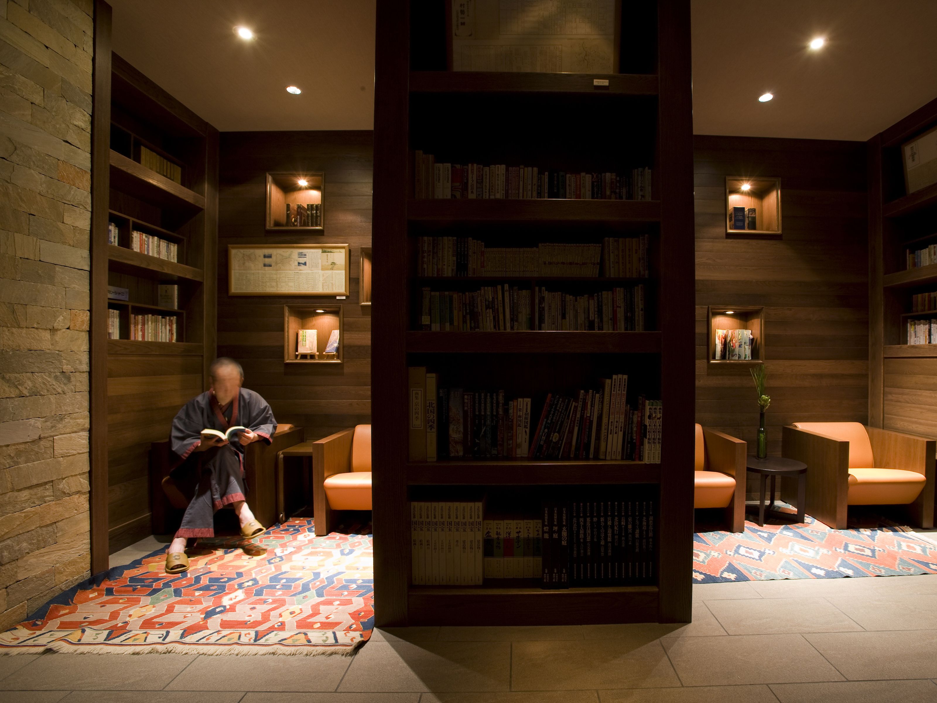 A library with bookshelves, a person reading, and a patterned carpet.