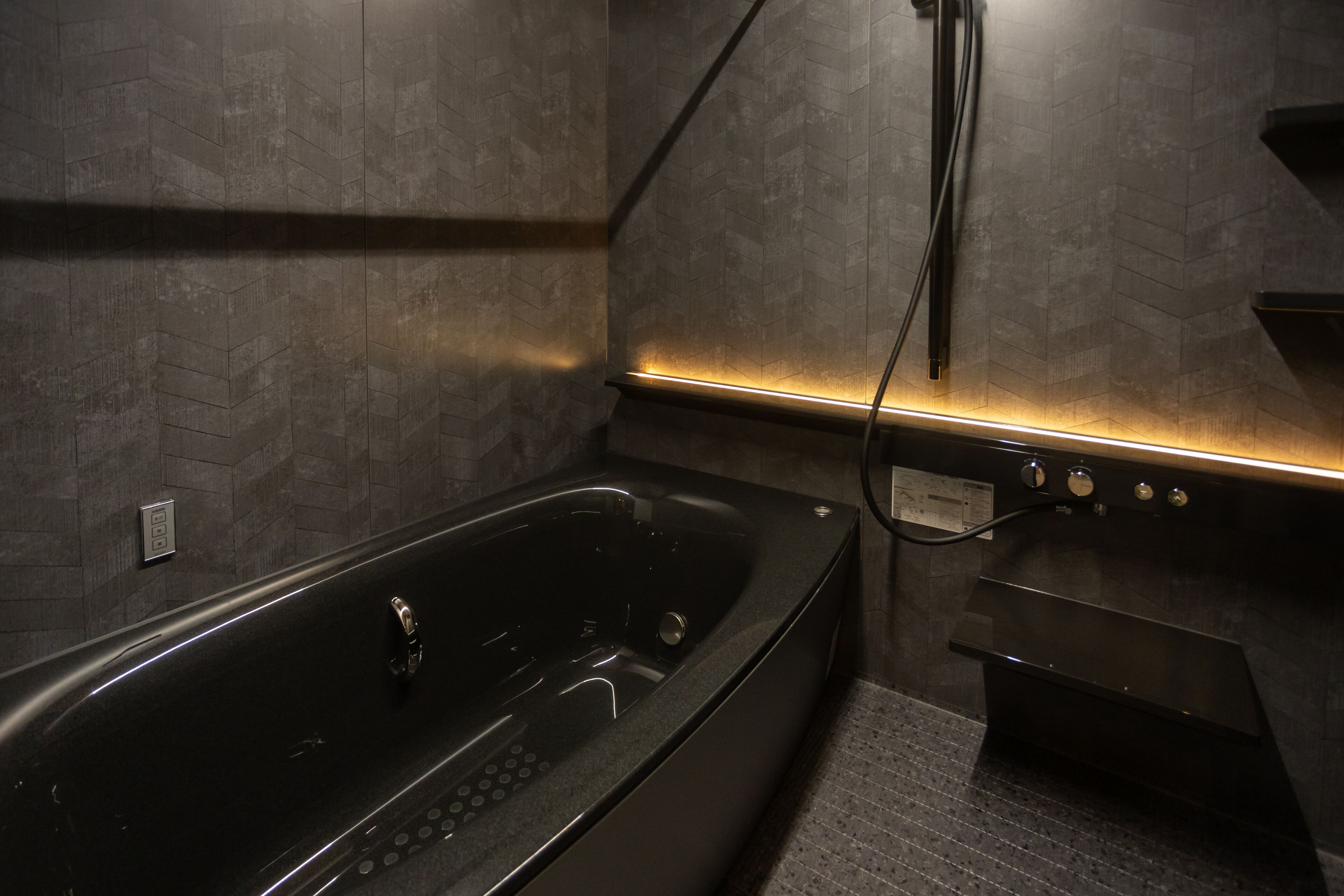 Un baño moderno con una bañera negra grande, ducha empotrada y un lavabo pequeño.