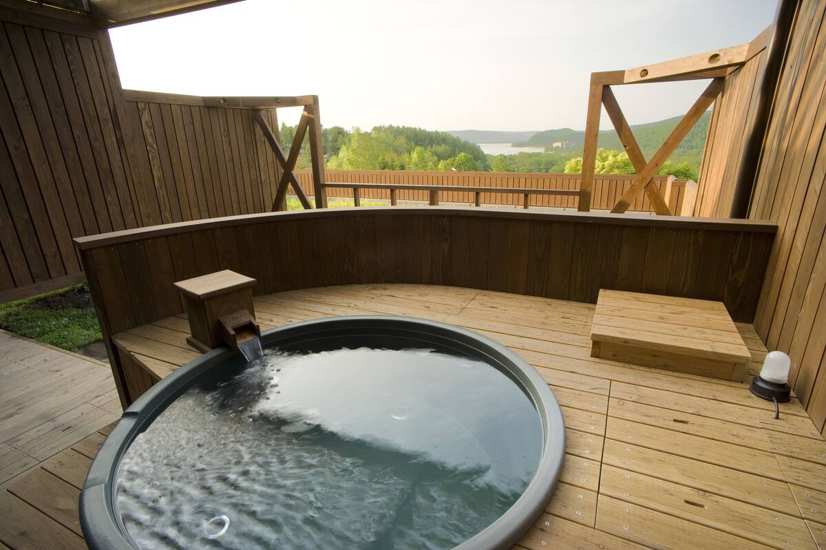 Un jacuzzi en una terraza de madera con vista a un lago y colinas.