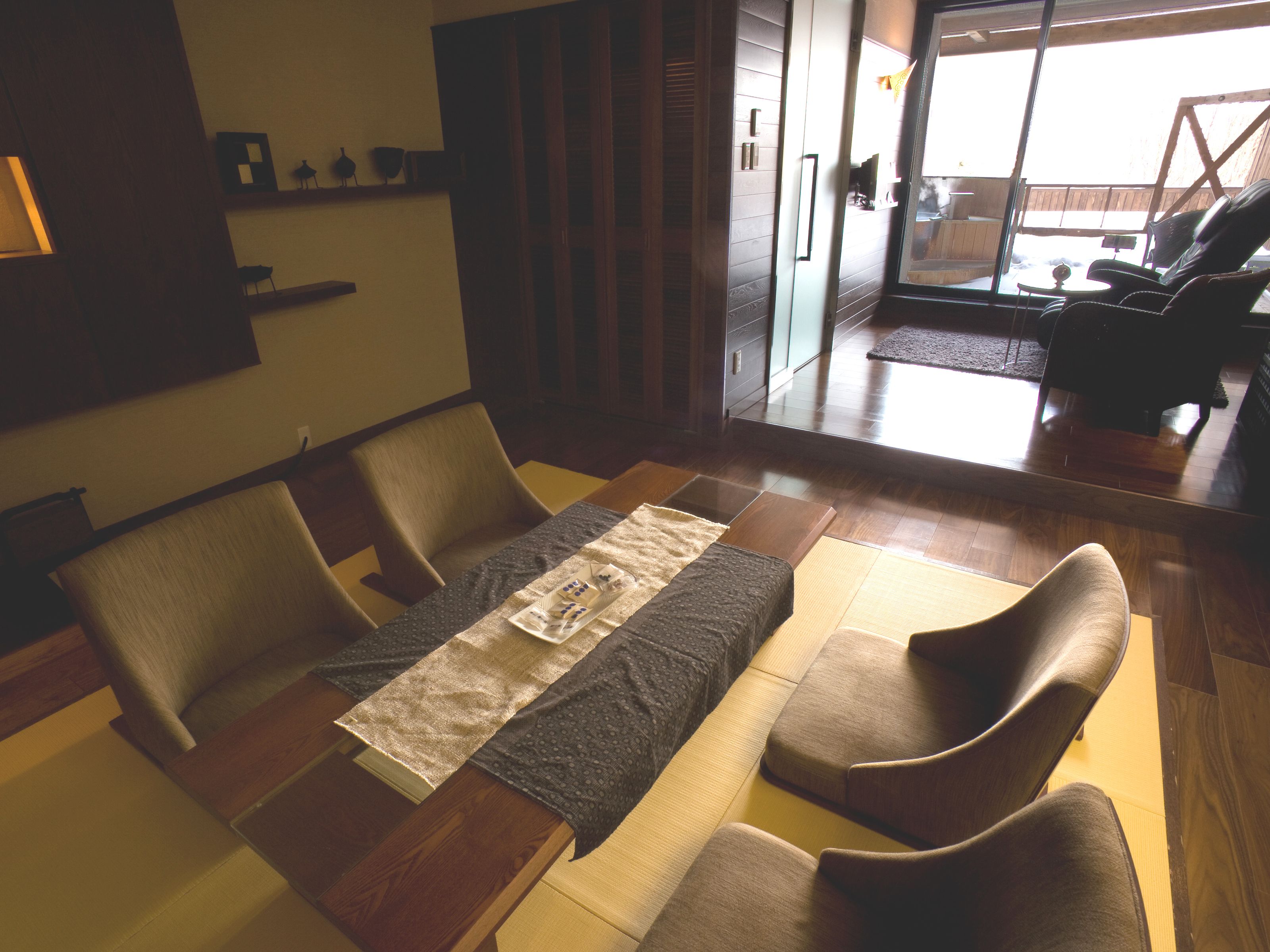 A modern living room with a sofa, chairs, and a coffee table. There is a sliding door leading to a balcony.