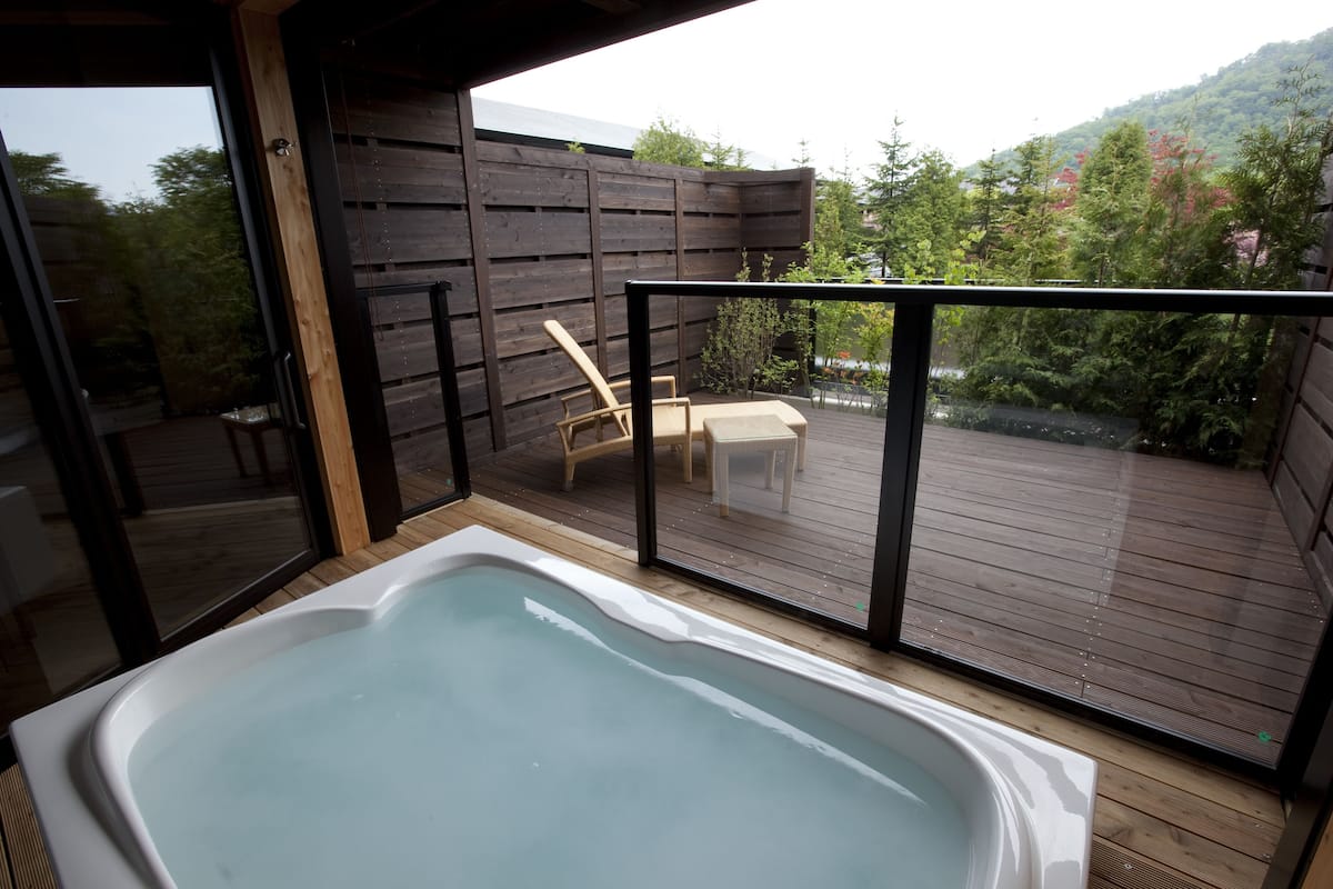 Un jacuzzi en una terraza de madera con vista a un jardín y árboles.