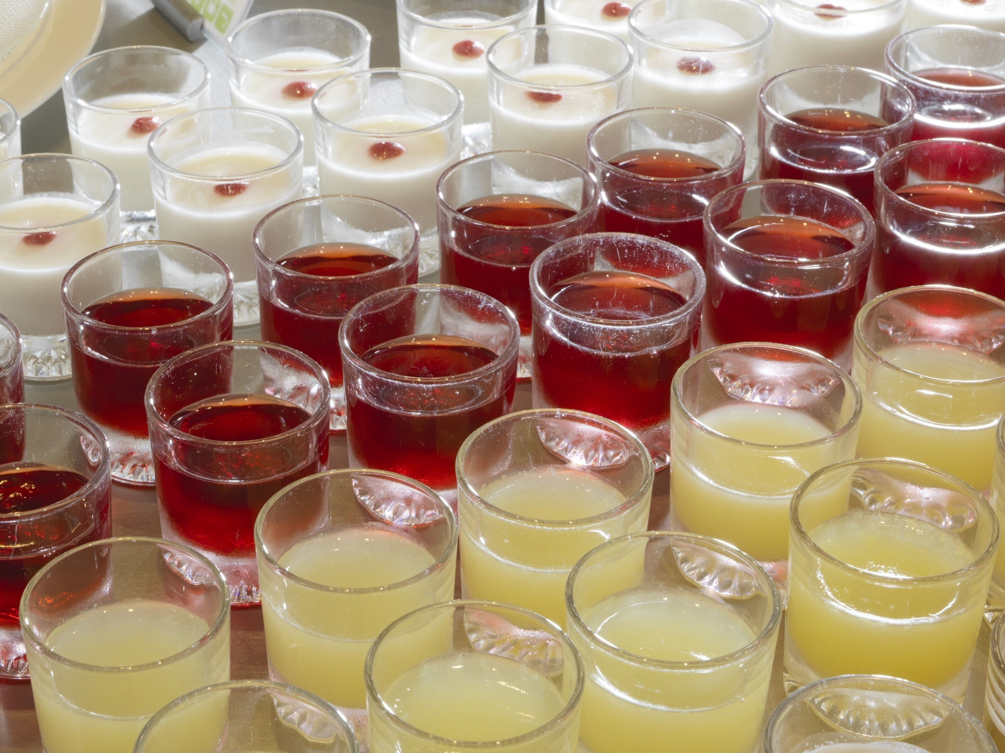 Variedad de bebidas en vasos, incluyendo bebidas rojas, blancas y amarillas, dispuestas sobre una mesa.