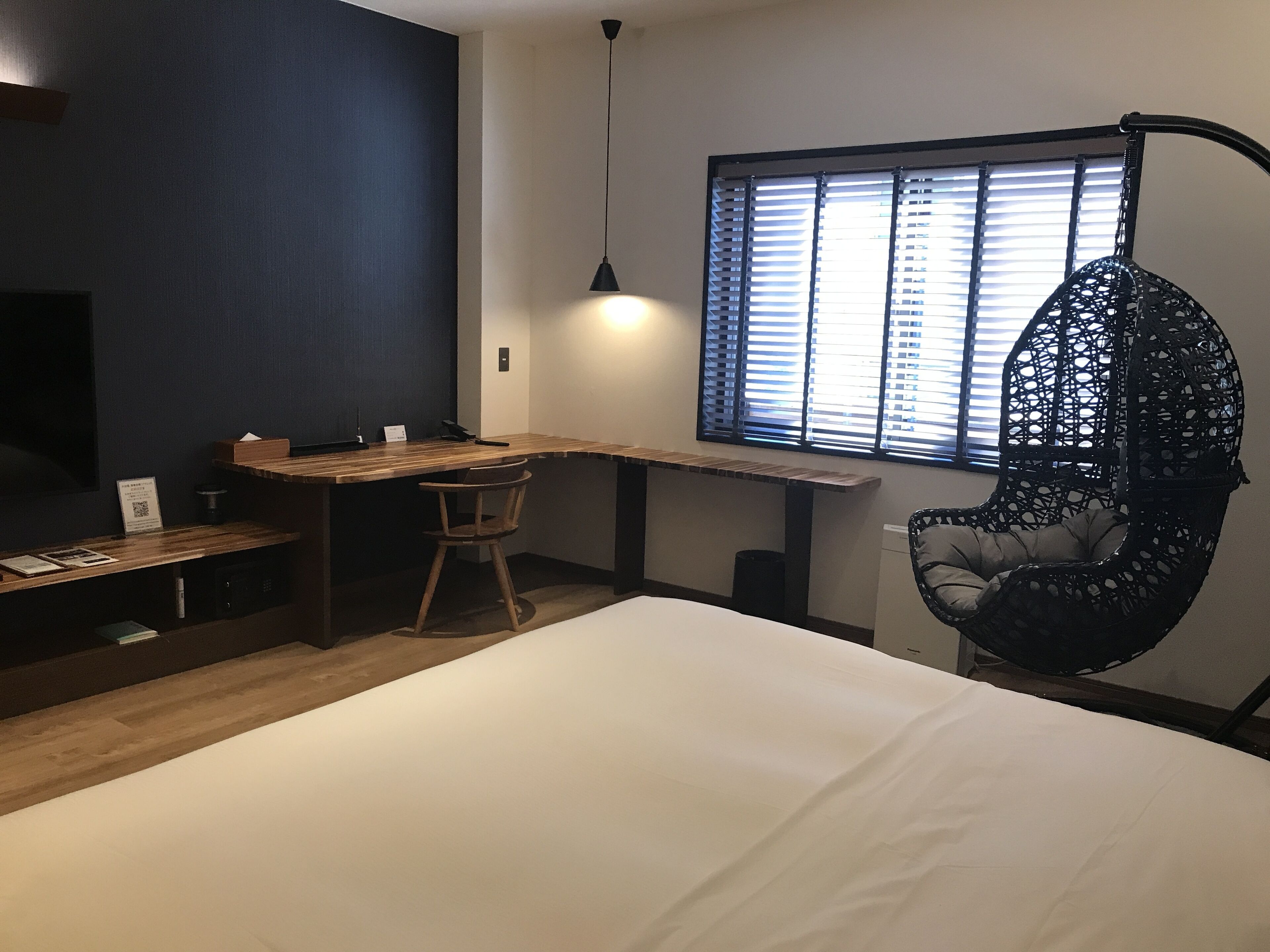 Een moderne slaapkamer met een houten bureau, een hangstoel en een groot bed.