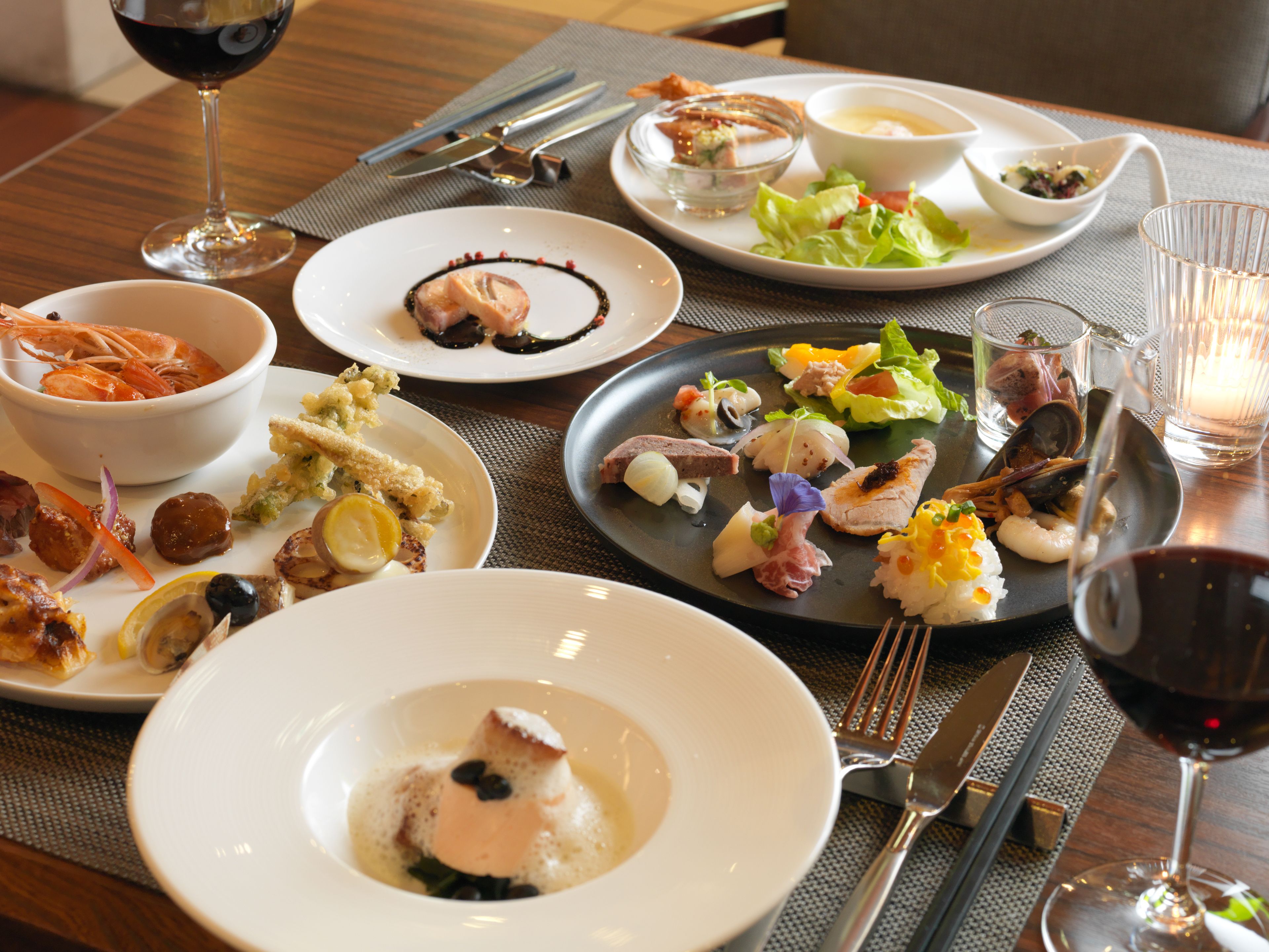 A table set with various dishes, including seafood, salads, and a dessert, with wine glasses and cutlery.