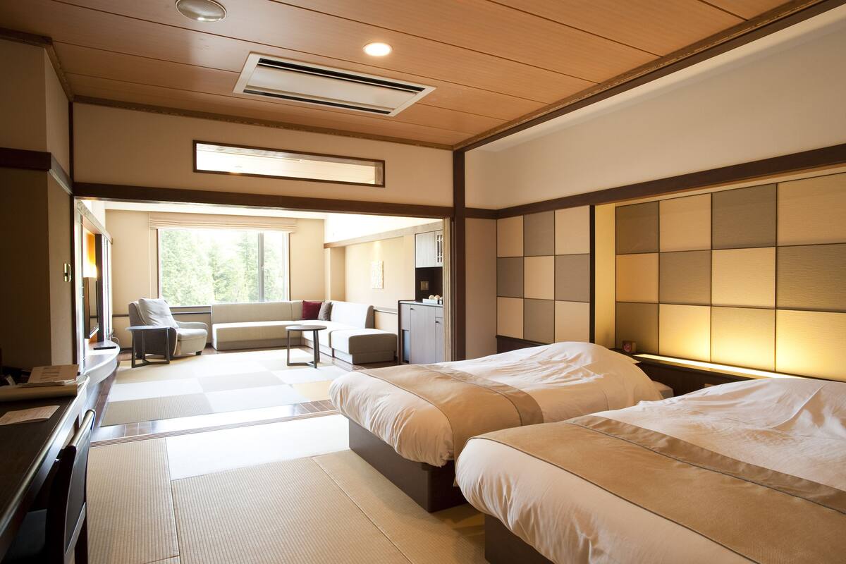Habitación de hotel con dos camas, un escritorio, una silla, un sofá y vistas al exterior.