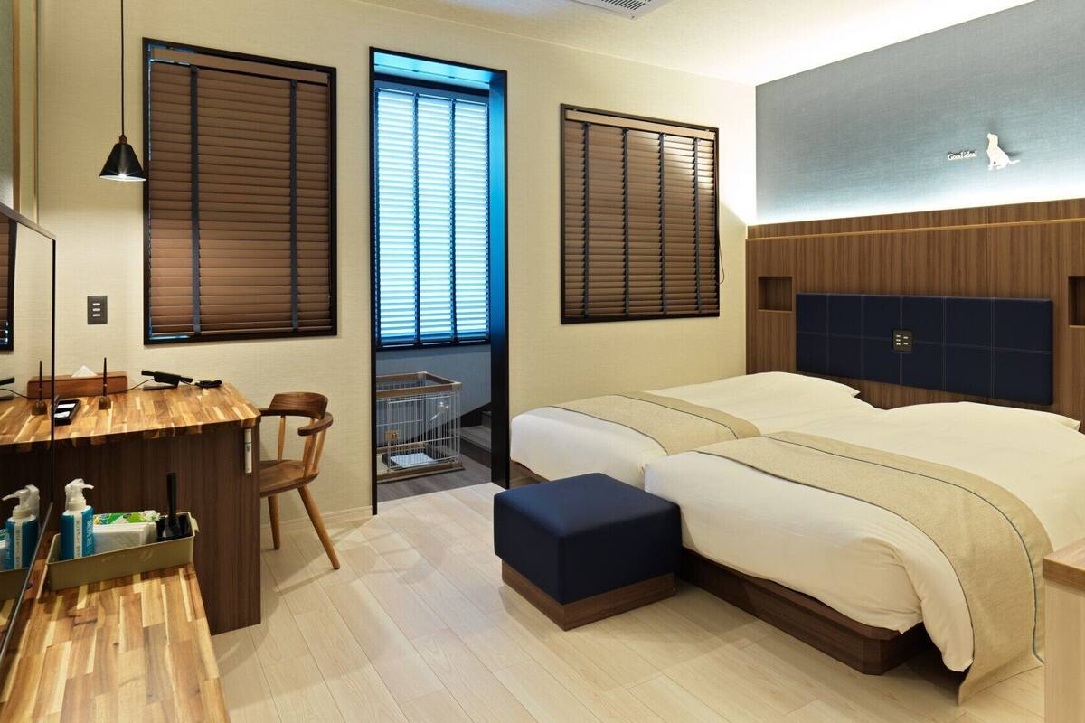 Una habitación de hotel con un escritorio de madera, dos camas, un balcón pequeño y un espejo grande.